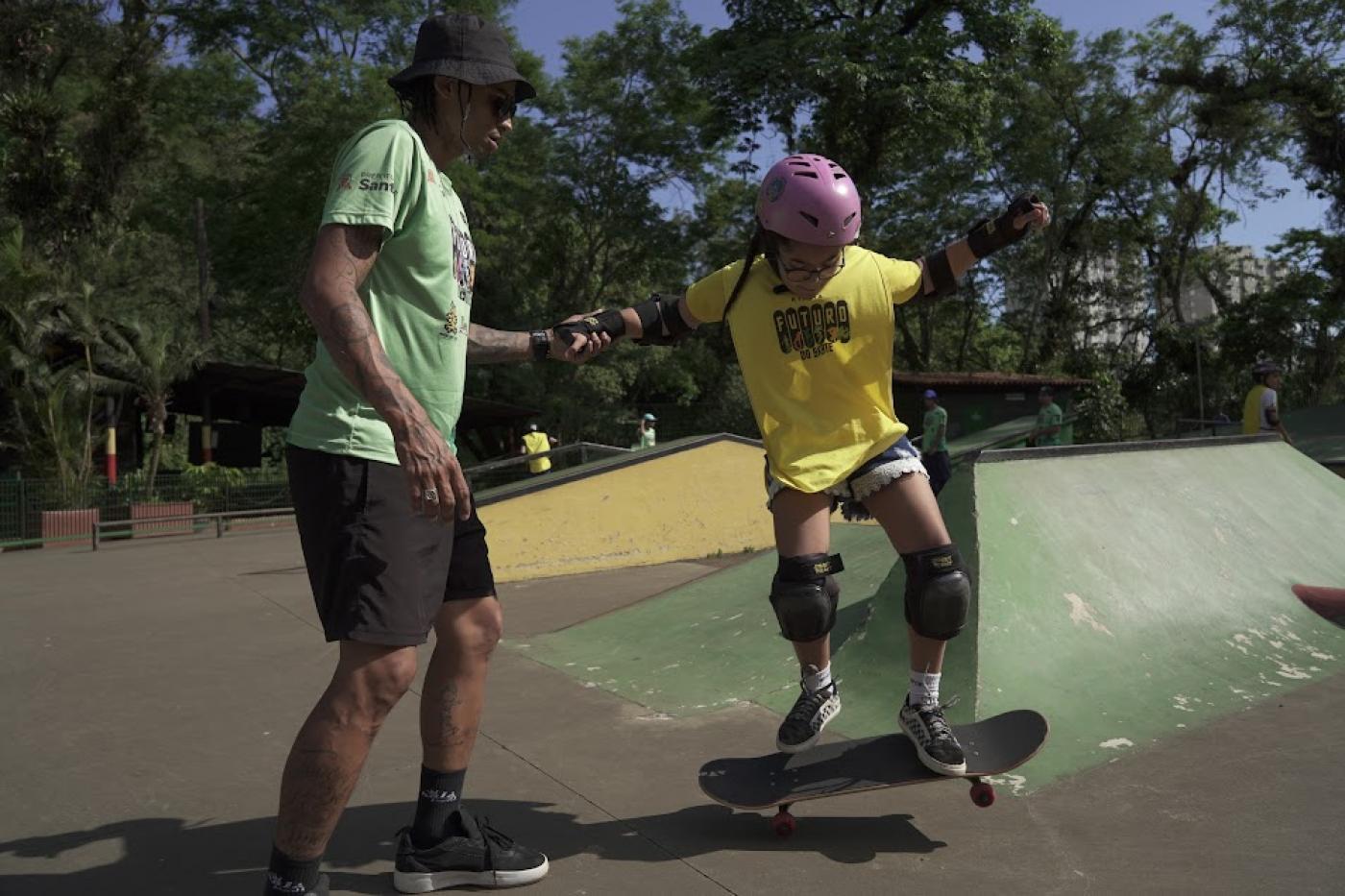 instrutor de skate dá apoio a alluna em pista. #paratodosverem 