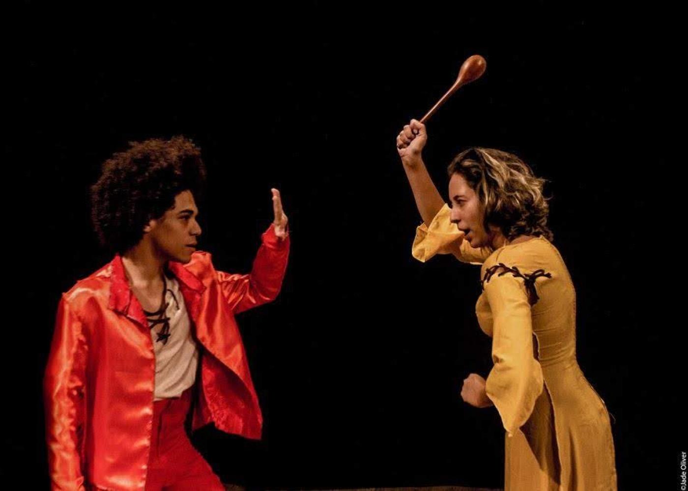 dois atores contracenando, uma mulher levanta uma colher de pau. #paratodosverem