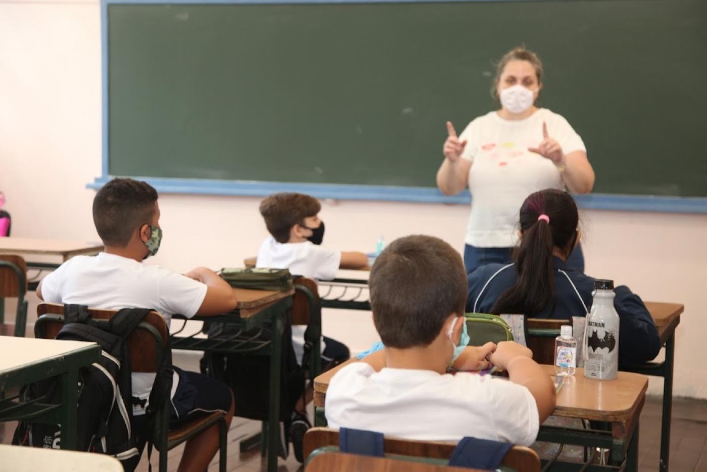 Professora na frente e alunos sentados assistindo a aula #paratodosverem