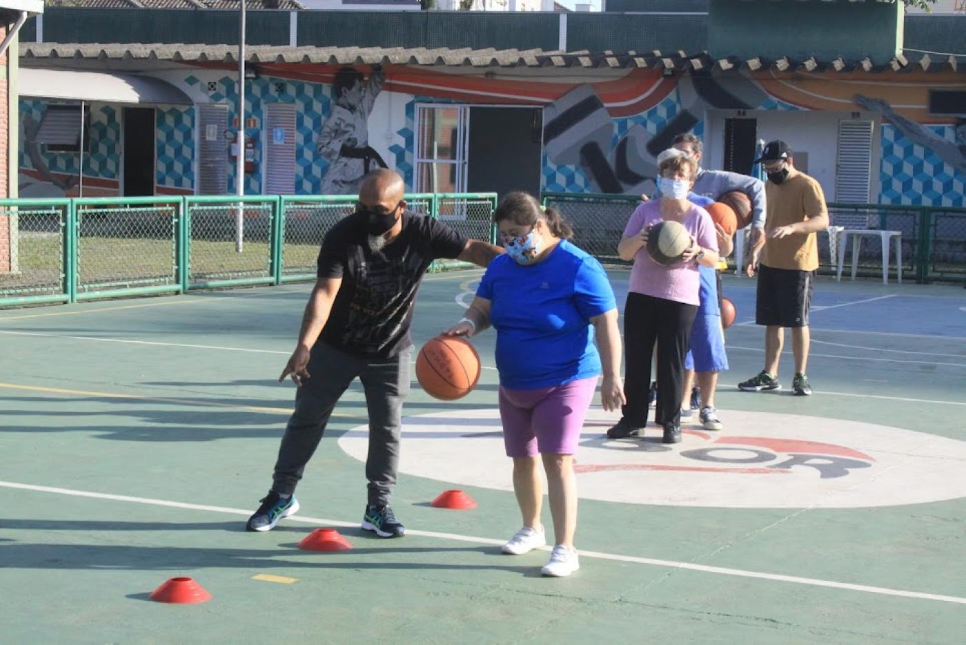 professor está orientando menina que bate bola de basquete. A quadra está com marcações por onde ela tem que ultrapassar. #paratodosverem