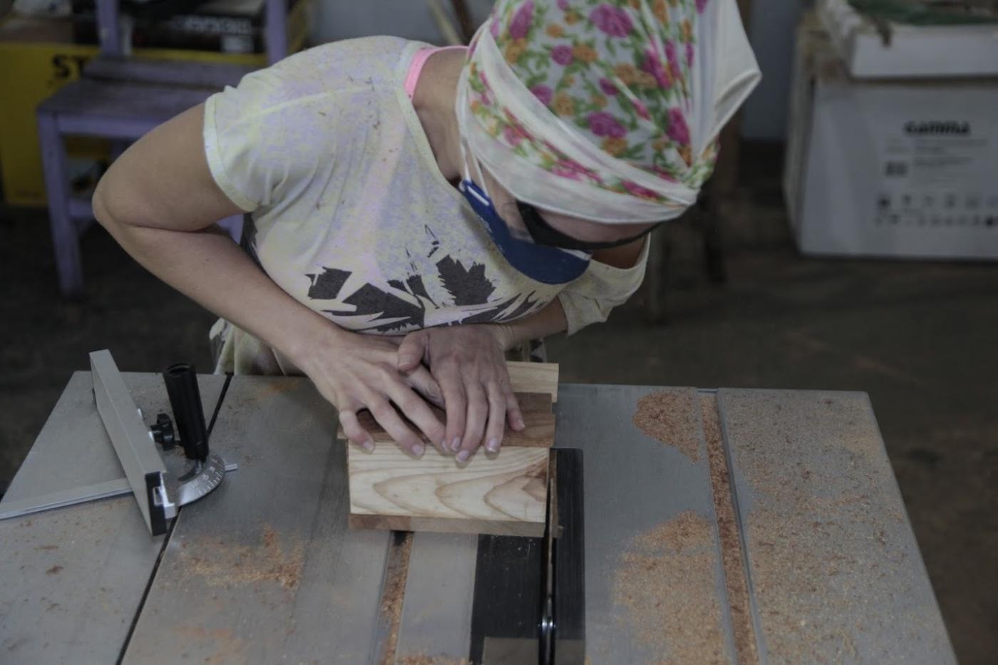 mulher está cortando uma peça de madeira em mesa de marcenaria. #paratodosverem 