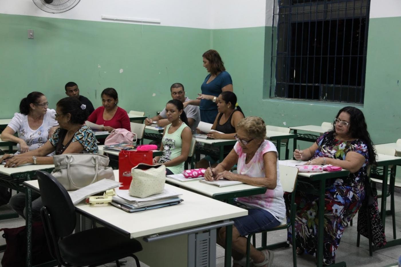 Sala de aula com adultos e a professora em pé. #paratodosverem
