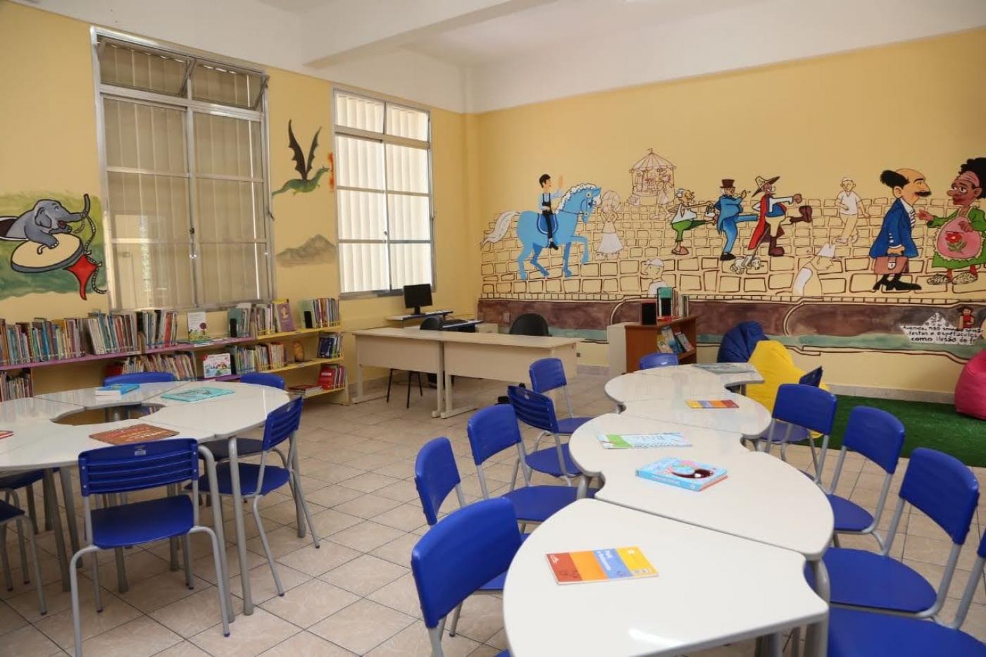 Interior de classe com pintura artística nas paredes. Mesas e cadeiras. #paratodosverem