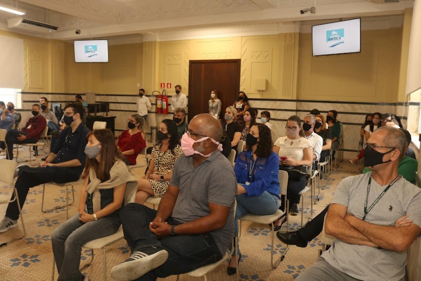 Servidores sentados assistindo apresentação #paratodosverem