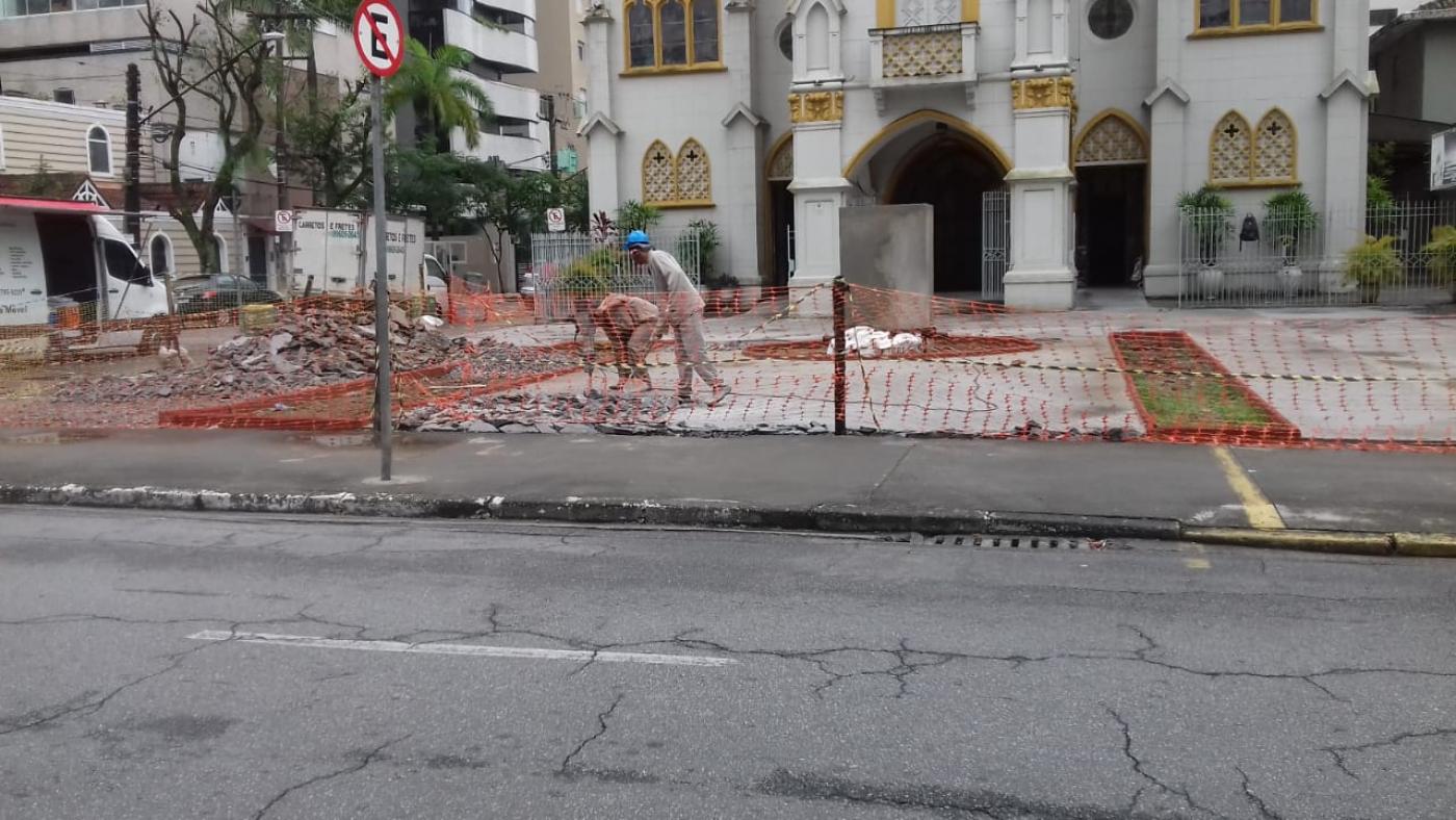 Trabalhadores quebram piso em praça com igreja ao fundo #paratodosverem