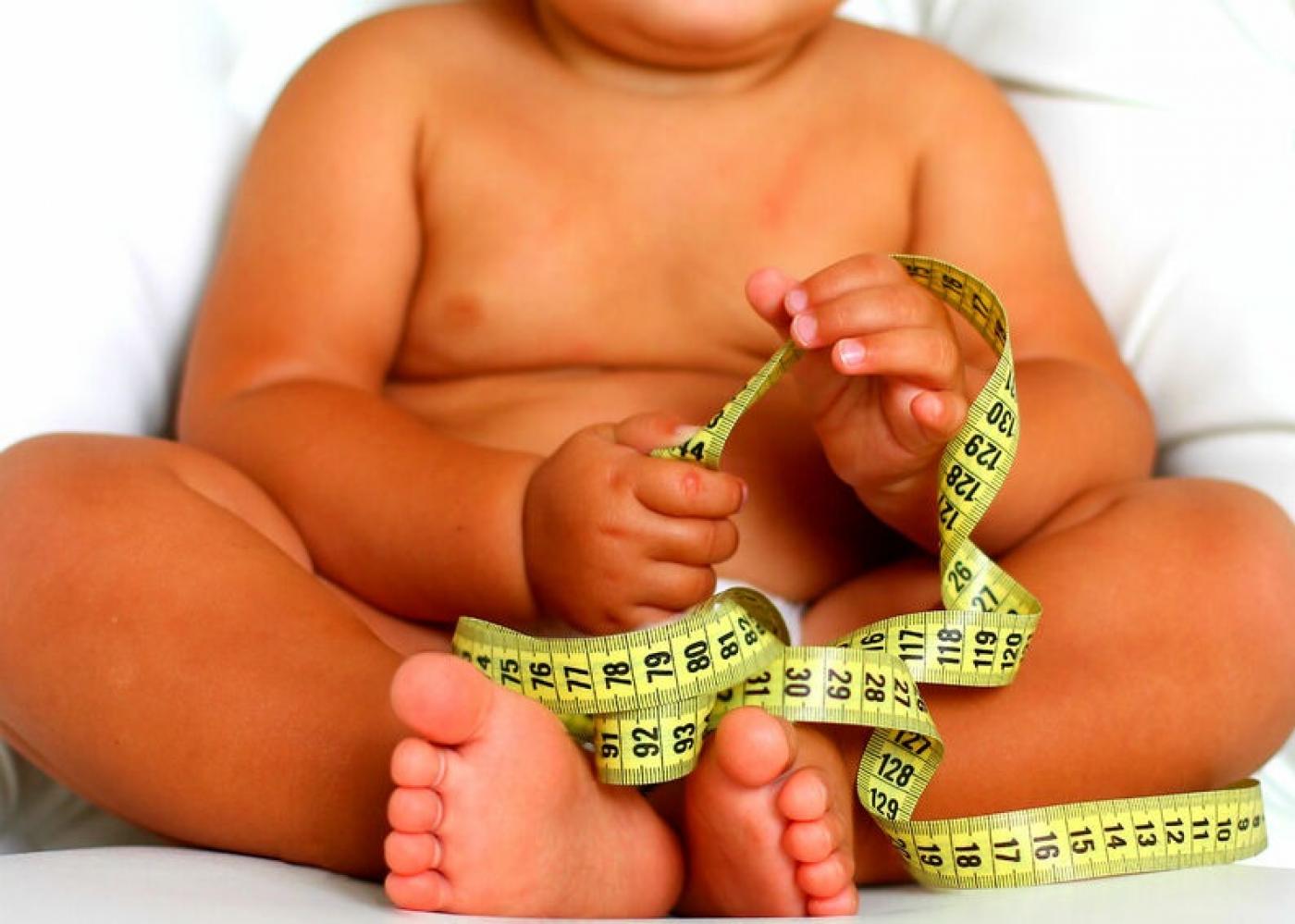 bebê obeso segura fita métrica.  #paratodosverem 