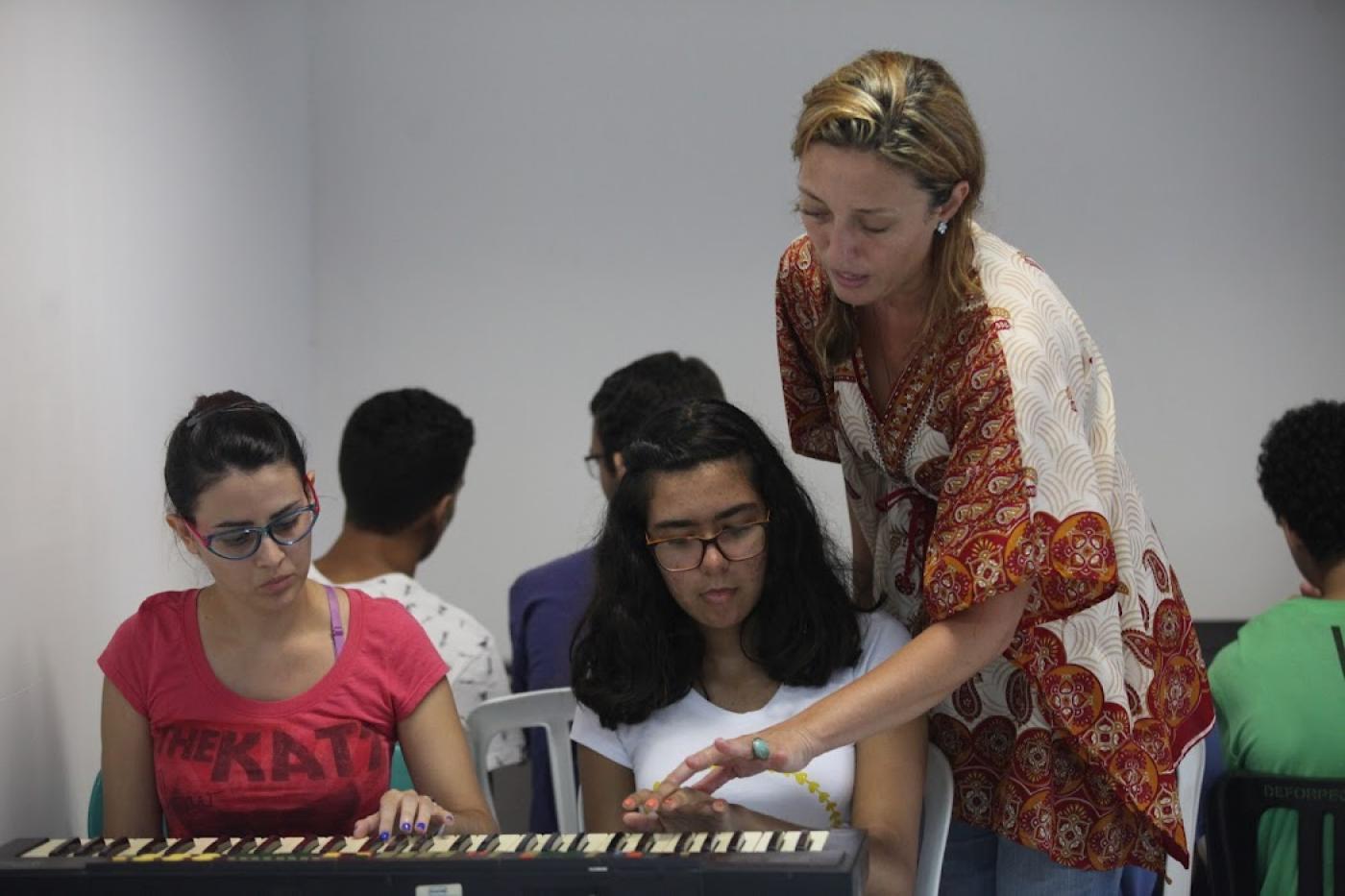 Mulher orienta alunos tocando no piano #paratodosverem