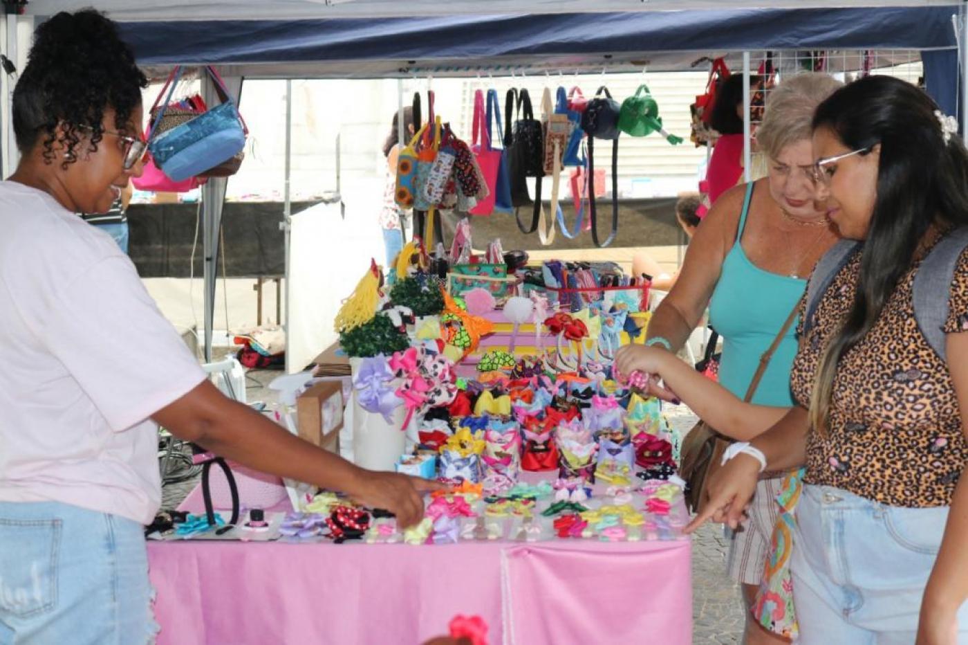 Pessoas olham produto em feira #paratodosverem 