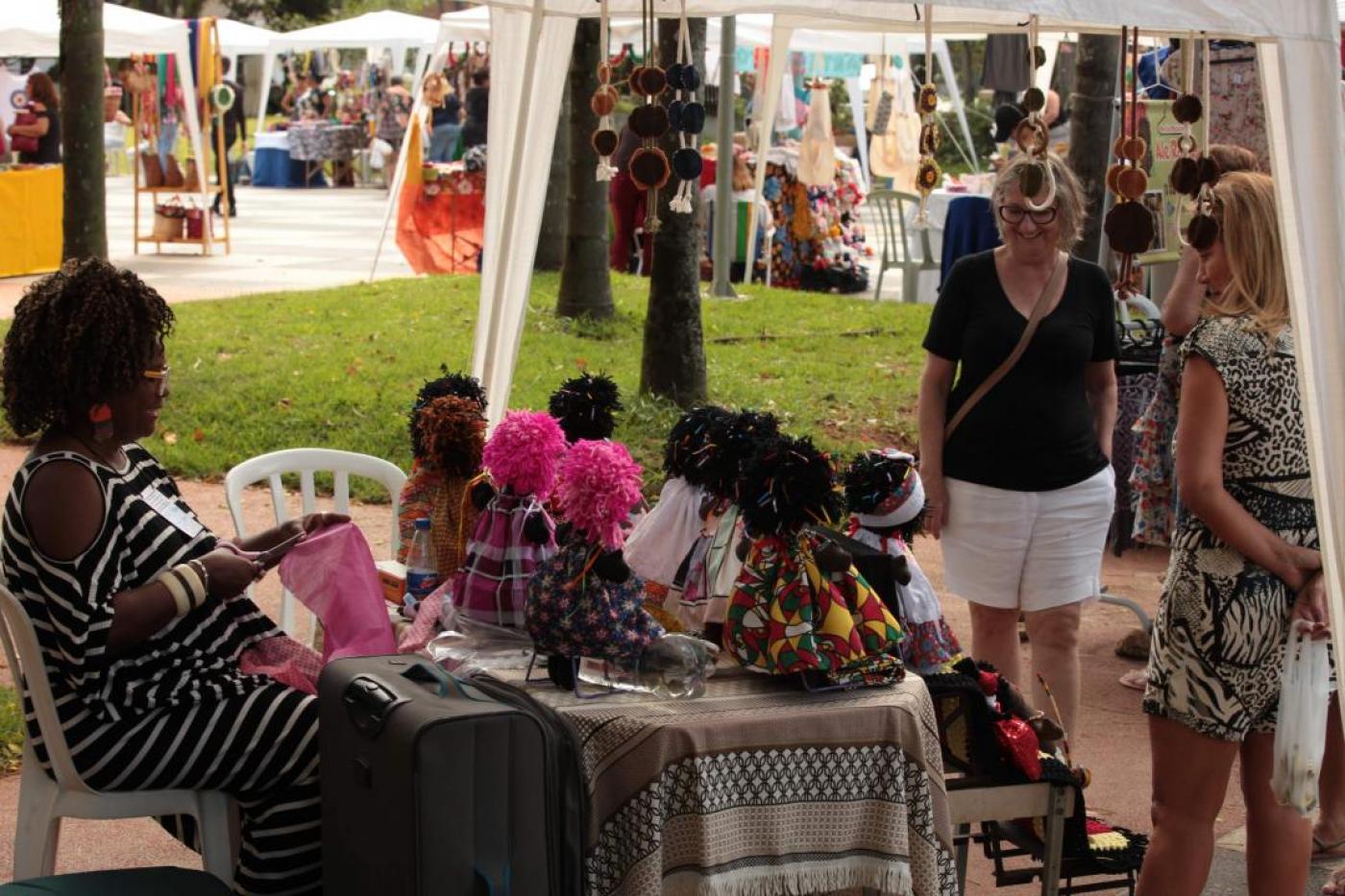 Pessoas observam barraca com bonecas afro #paratodosverem