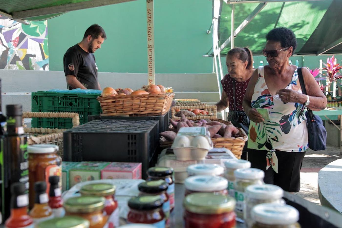 Mulheres observam produtos em barraca. #pratodosverem