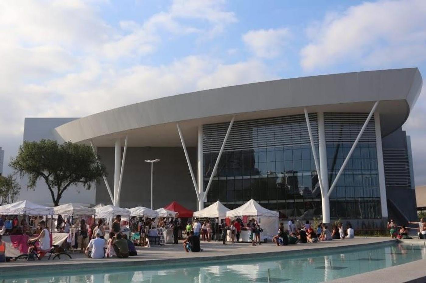 Foto da fachada do Santos Convention Center com várias barraquinhas e pessoas na frente. #paratodosverem