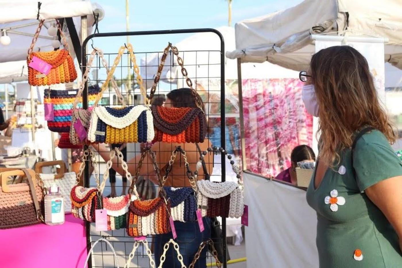 Mulher observa bolsas penduradas em barraca. #paratodosverem