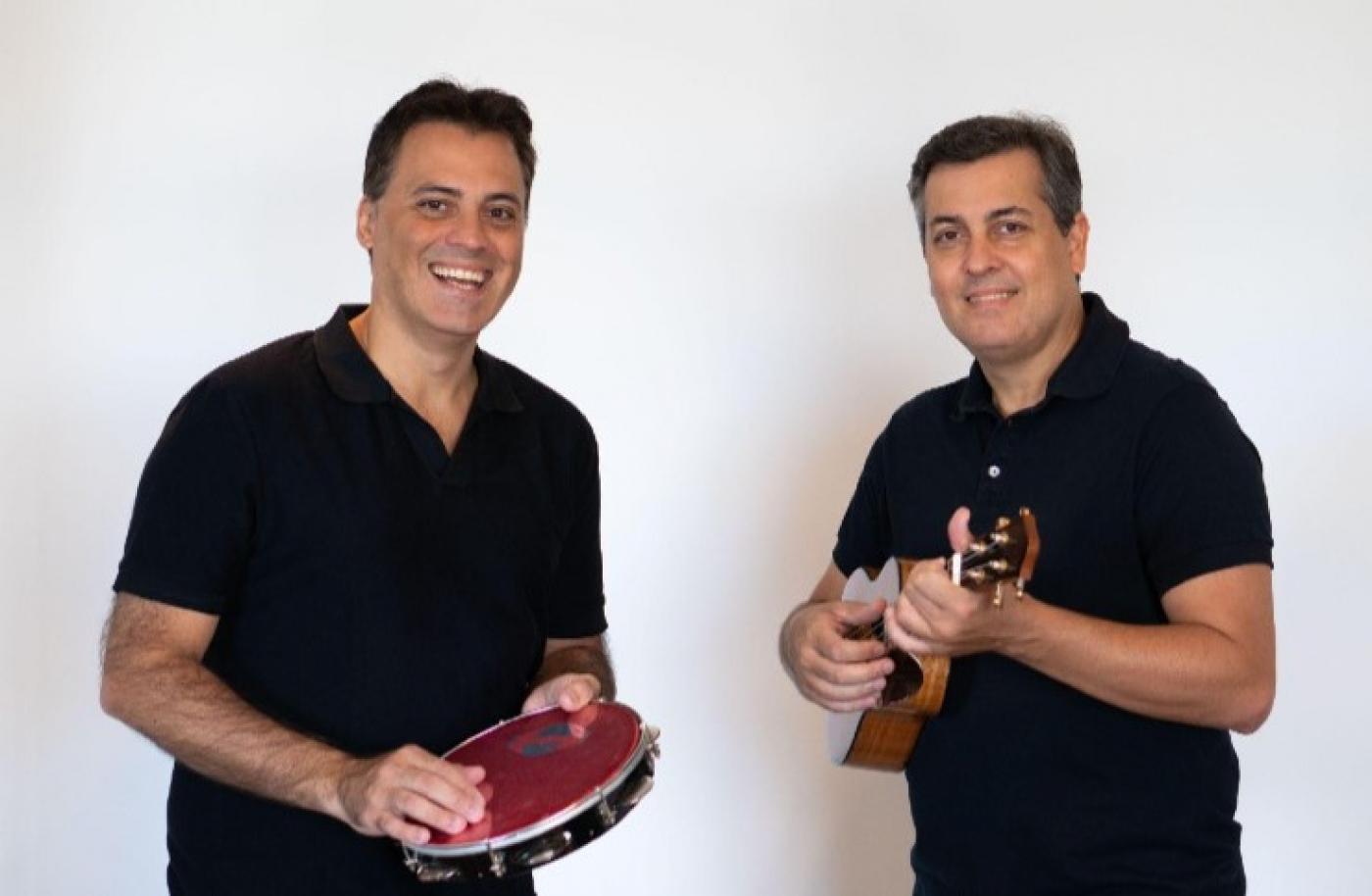 dois homens estão lado a lado. Um toca pandeiro e o outro, cavaquinho