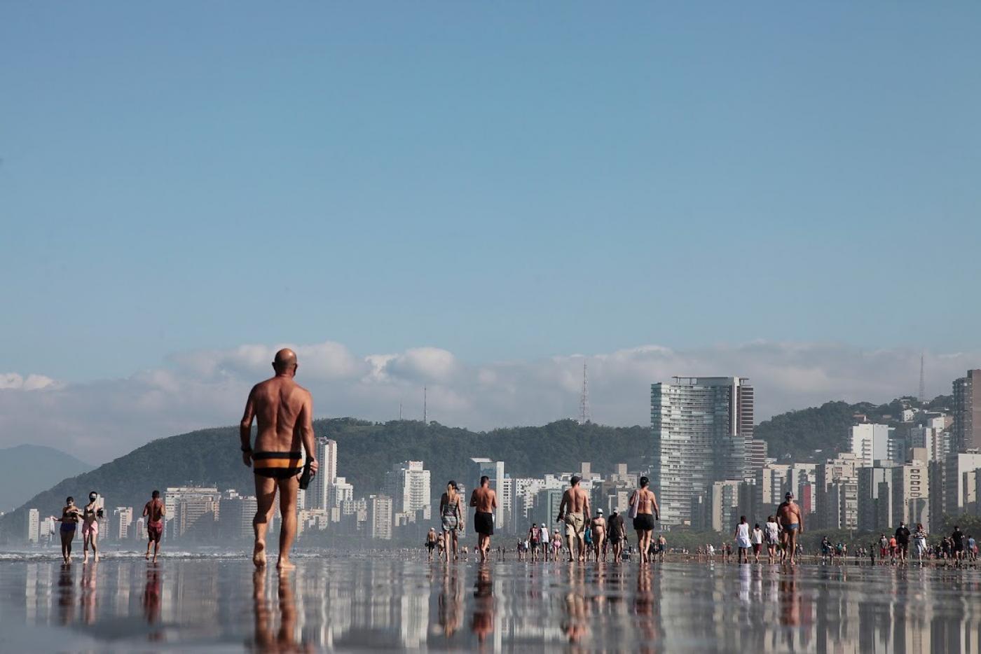 Pessoas andando na beira da água em praia de Santos #paratodosverem