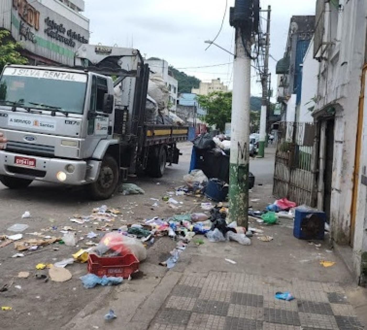 caminhão está parado em rua. Há muito lixo no chão em torno do imóvel. #paratodosverem