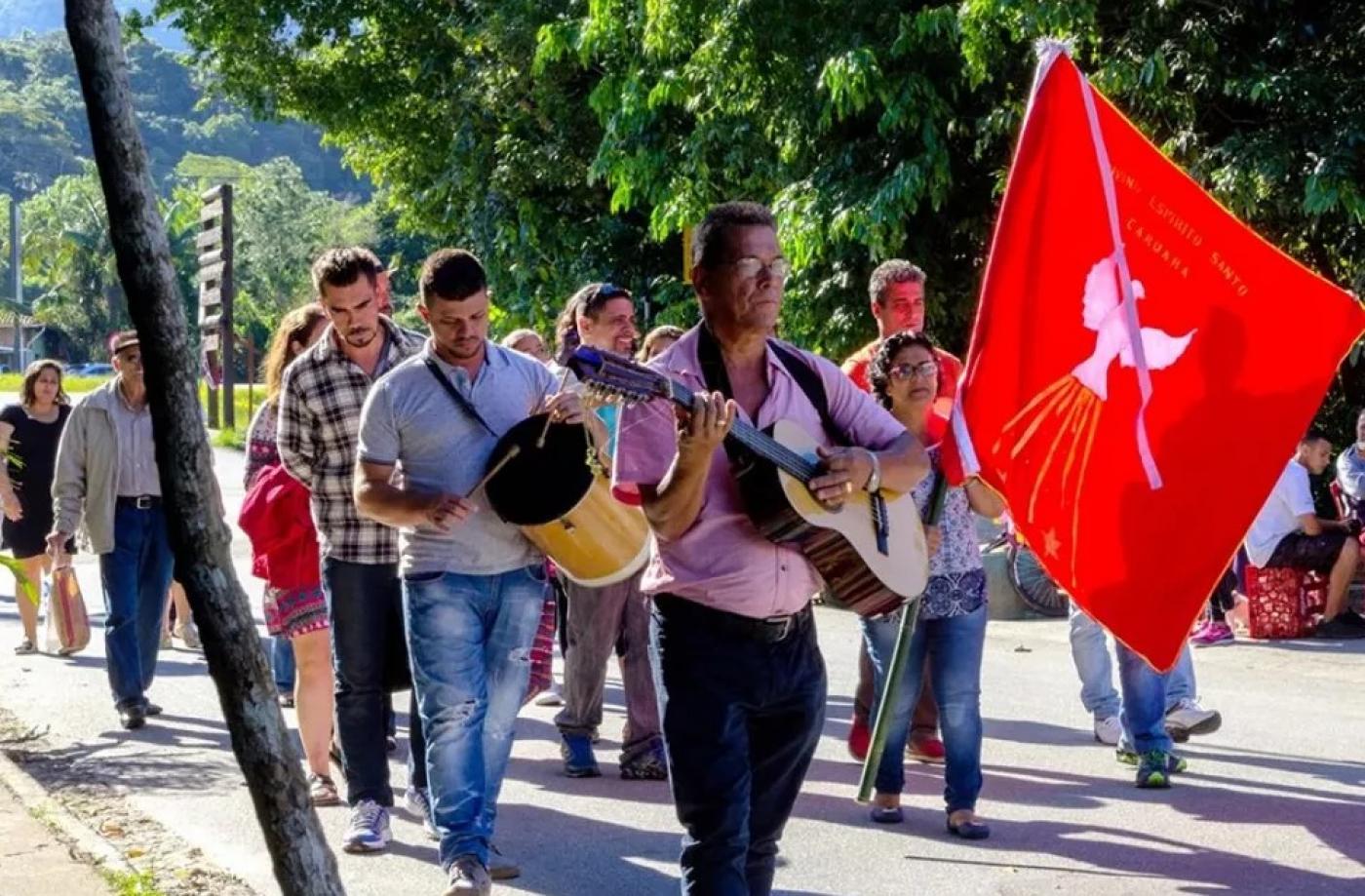 pessoas andando segurando bandeira e tocando instrumentos #paratodosverem