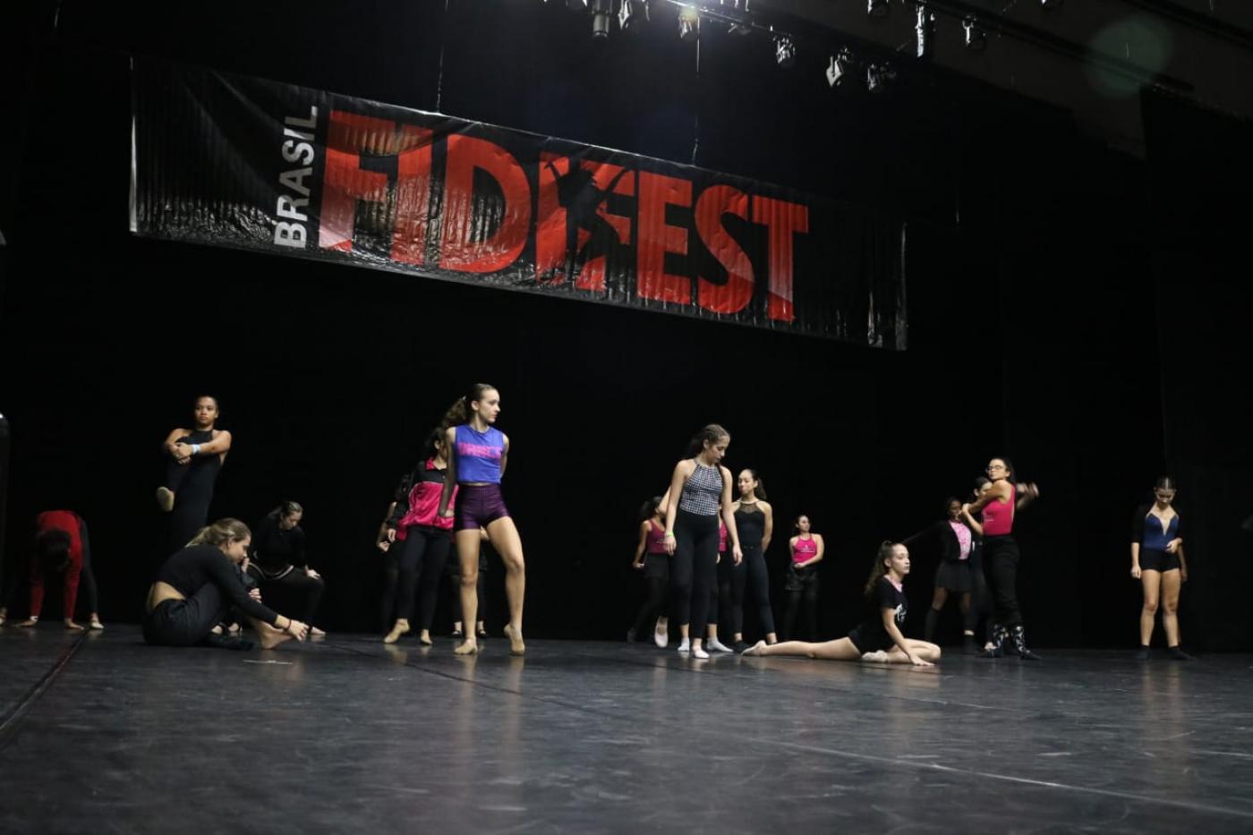 bailarinos estão no palco se movimentando. Ao fundo e no alto se lê fidifest brasil. #paratodosverem