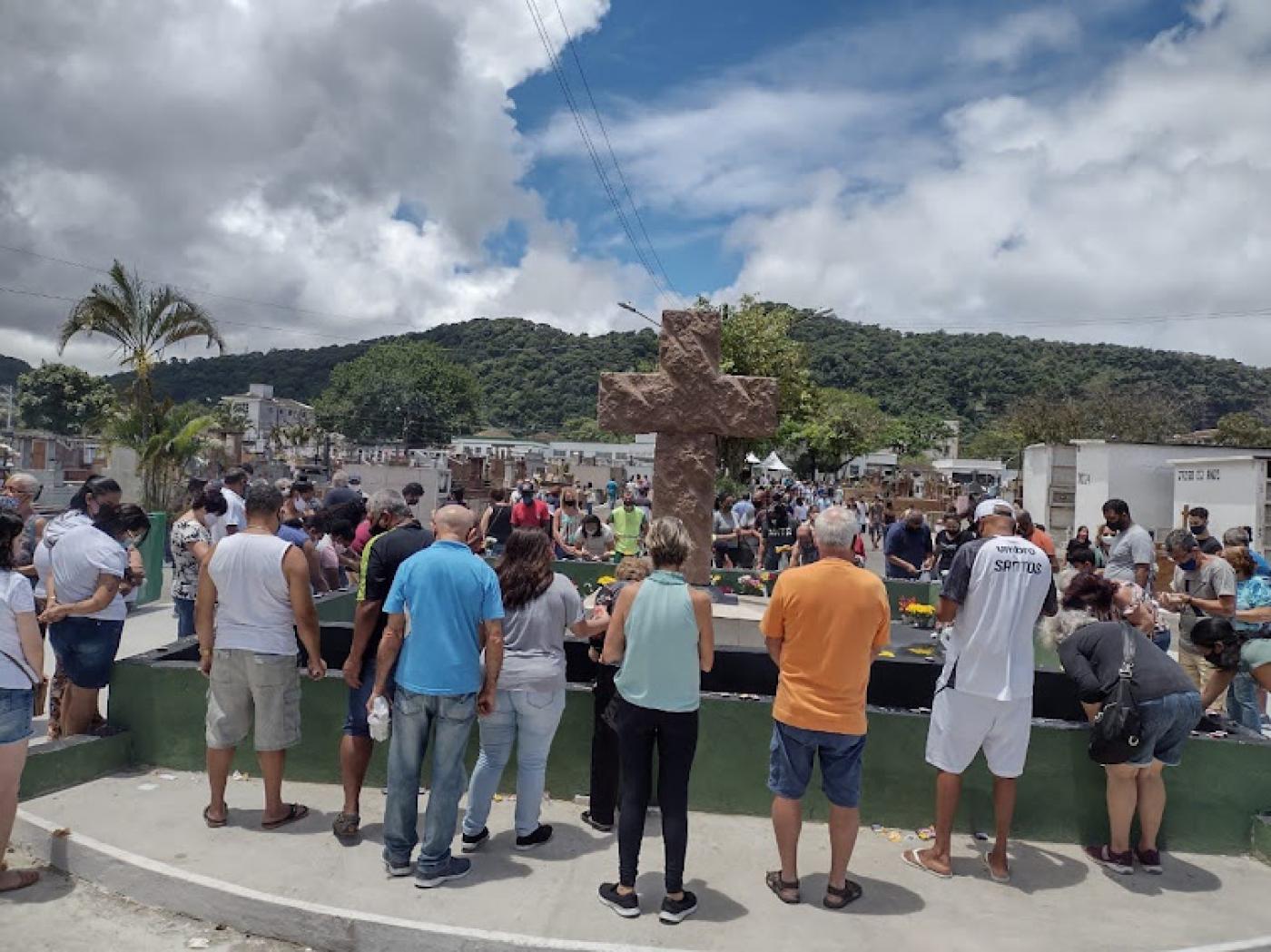 Pessoas rezando na frente de uma cruz no cemitério #paratodosverem