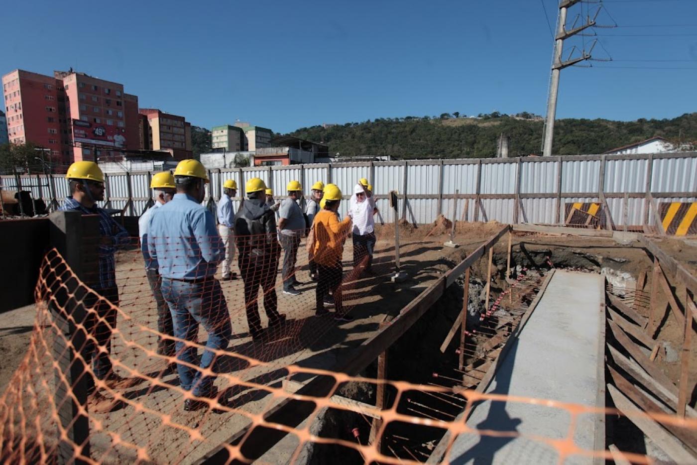 várias pessoas usando capacete estão olhando andamento de obra. #paratodosverem