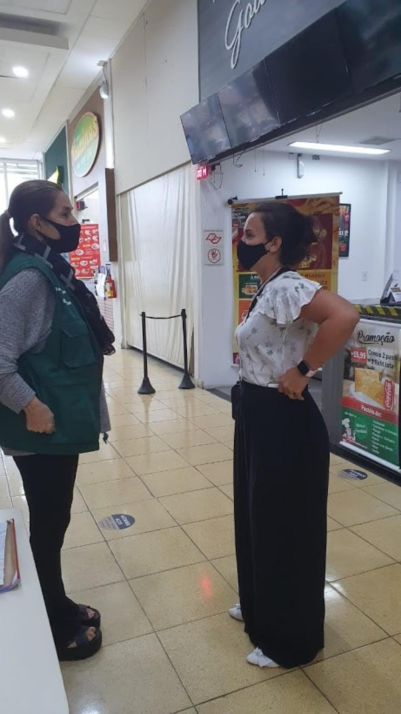 Fiscal conversa com mulher em área de alimentação de shopping