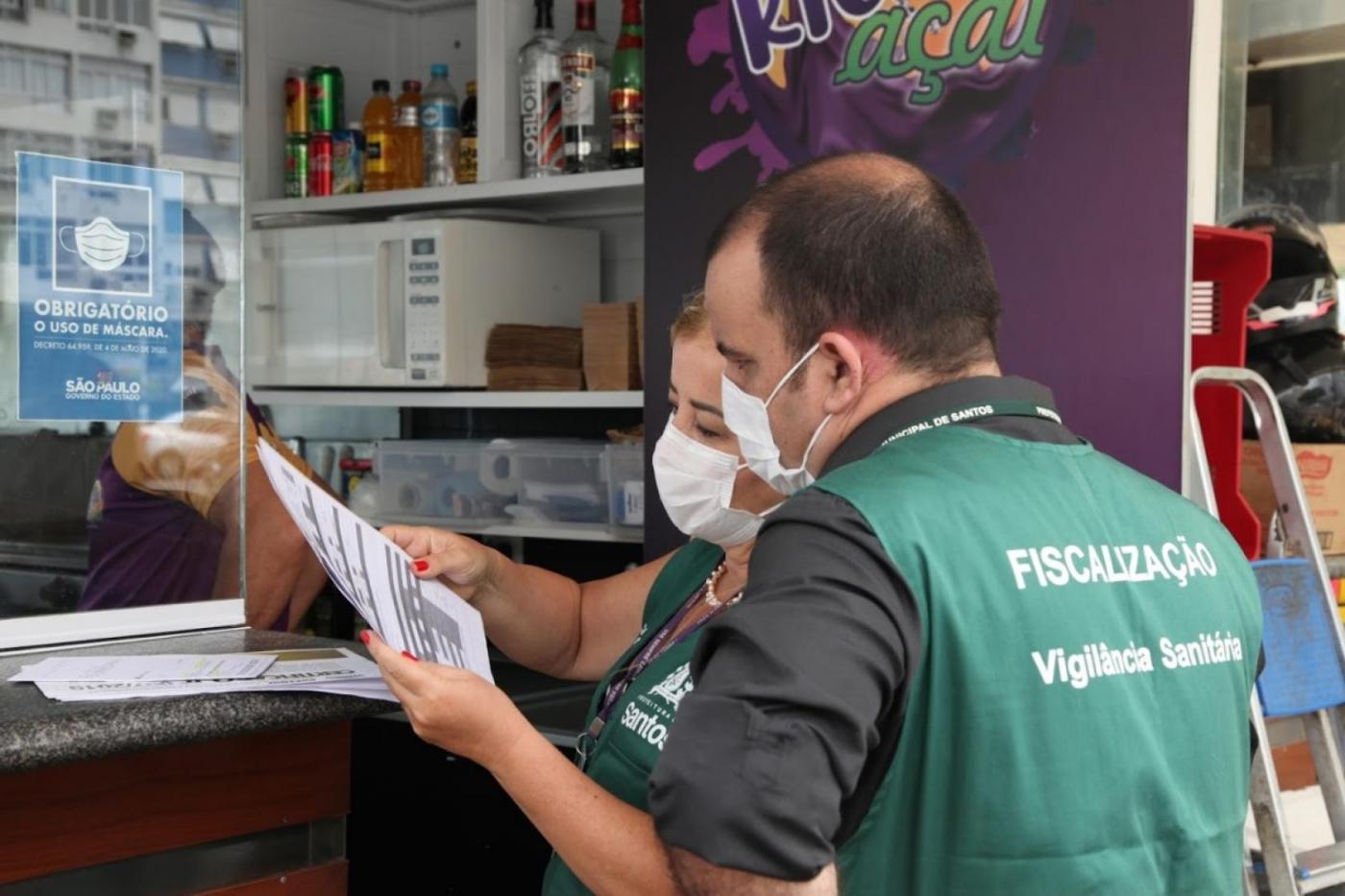 Fiscais observam documentação de comércio. #pracegover