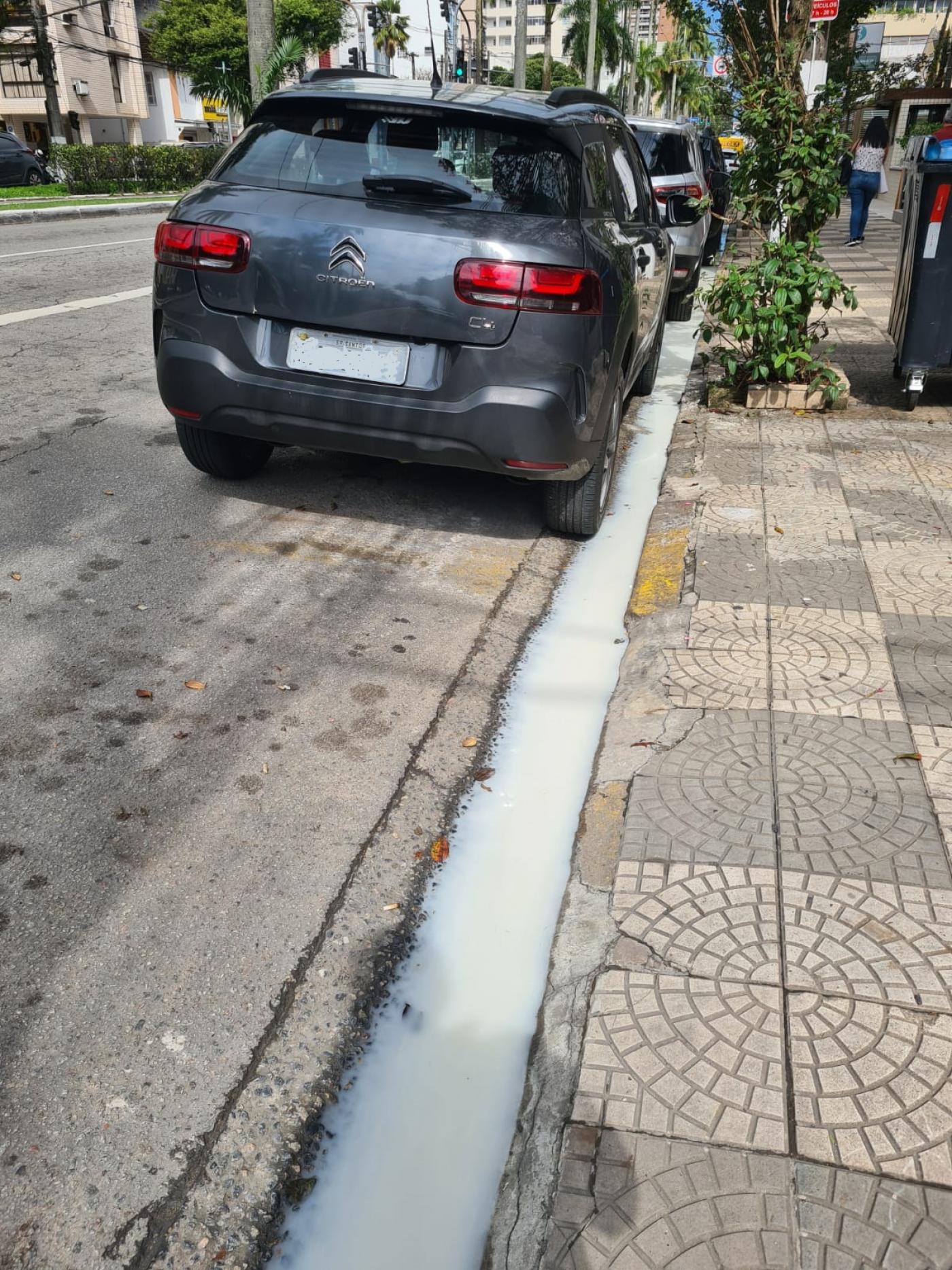 guia junto a sarjeta em avenida com água na cor branca, demonstrando o despejo irregular. Há um carro estacionado à frente. #paratodosverem 