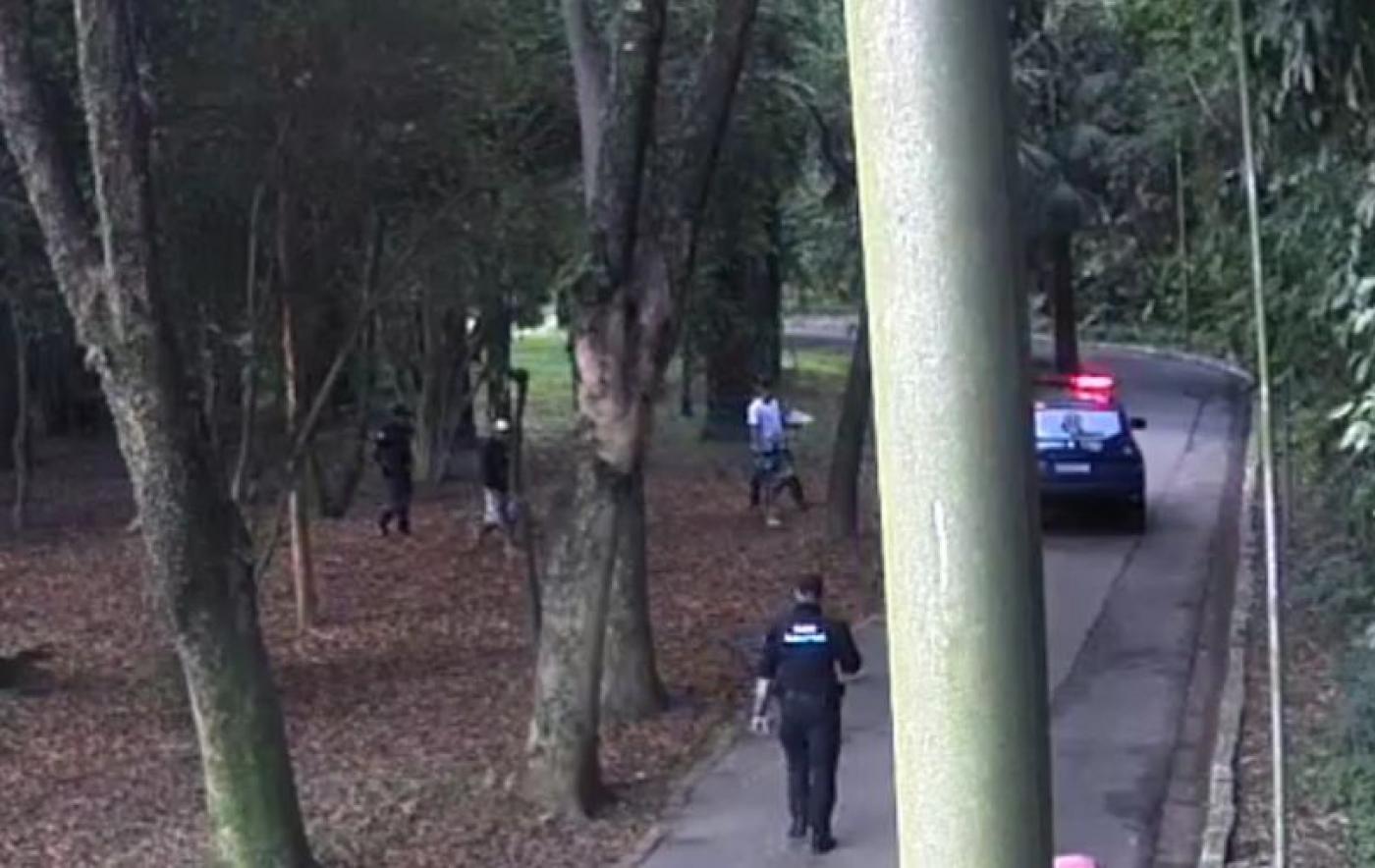 guarda municipal caminha em alameda na direção de homens num parque. à frente está uma viatura da corporação. #paratodosverem