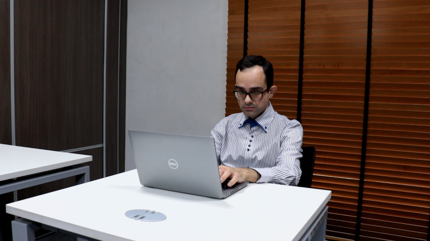 Rapaz de óculos e camisa social trabalha sentado diante de laptop. #pratodosverem
