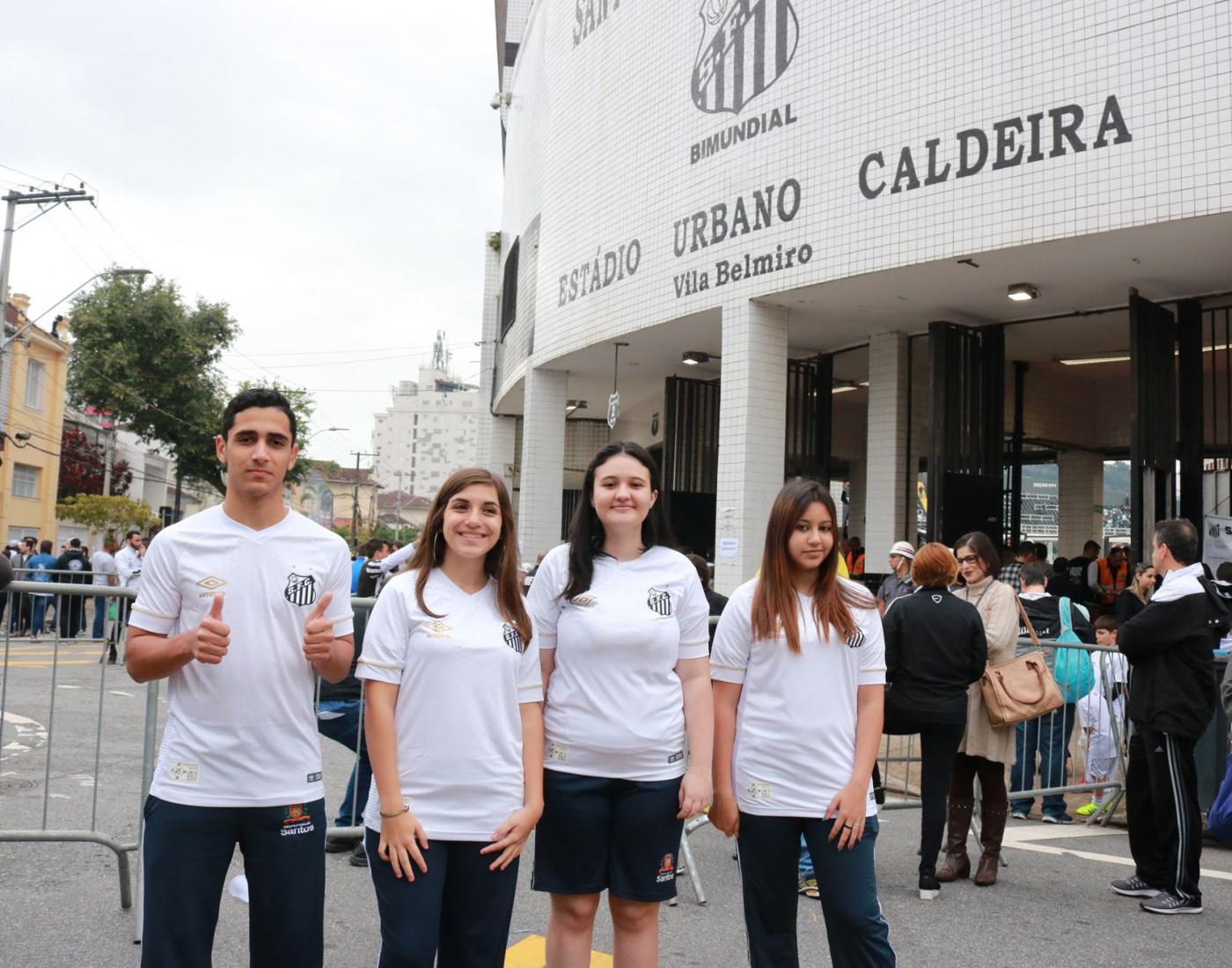 quatro alunos com camisas do santos posam na porta do estádio #pracegover
