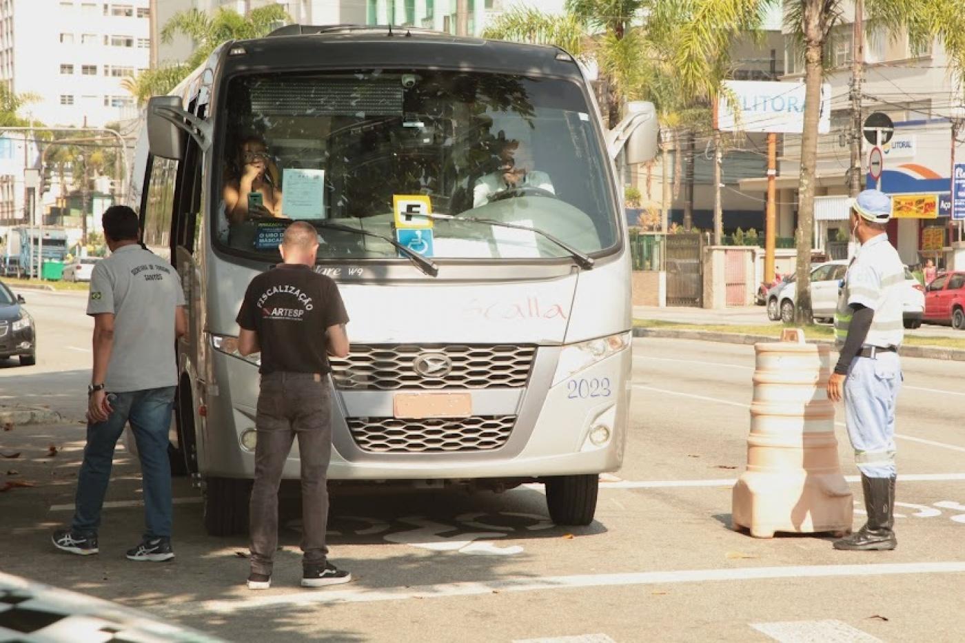 micro-ônibus está parado em avenida e três fiscais estão à frente. Eles são da Seectur, Artesp e CET-Santos 