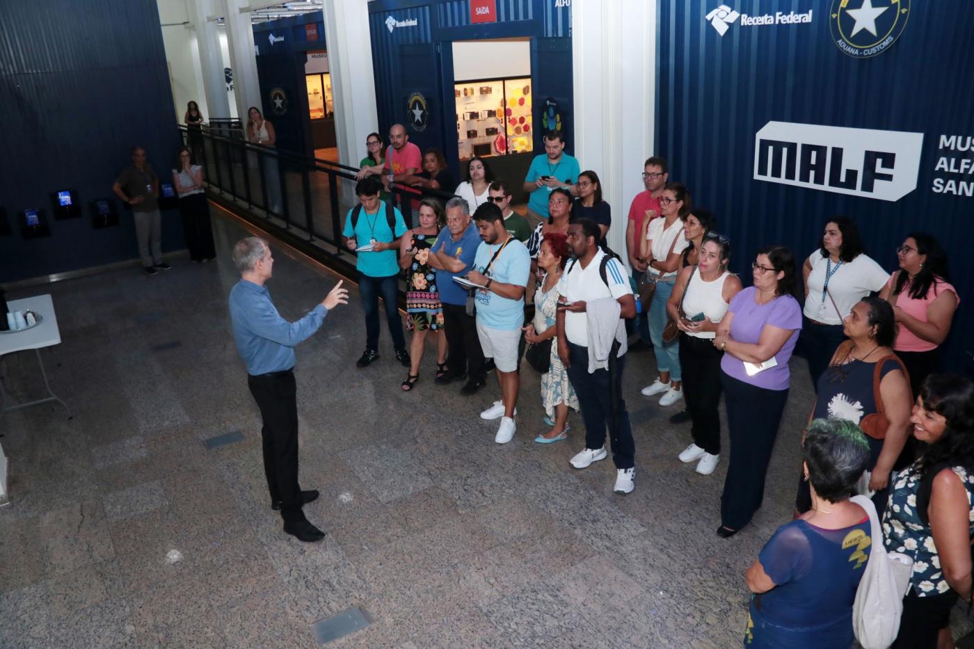 grupo de pessoas assiste homem falando dentro de museu. #paratodosverem 