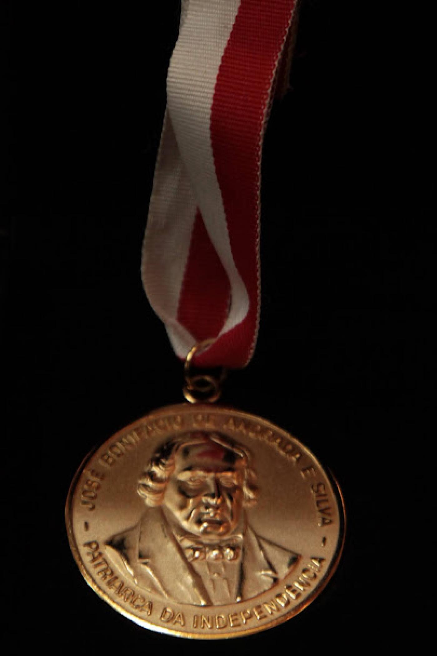 a medalha dourada, com o busto de josé bonifácio, sobre um fundo preto. #paratodosverem