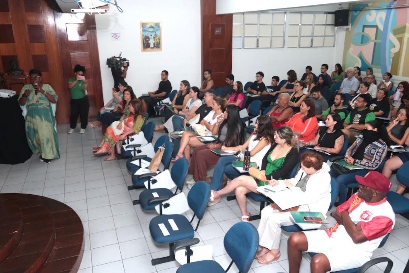 uma pessoa em pé de frente para uma plateia #paratodosverem