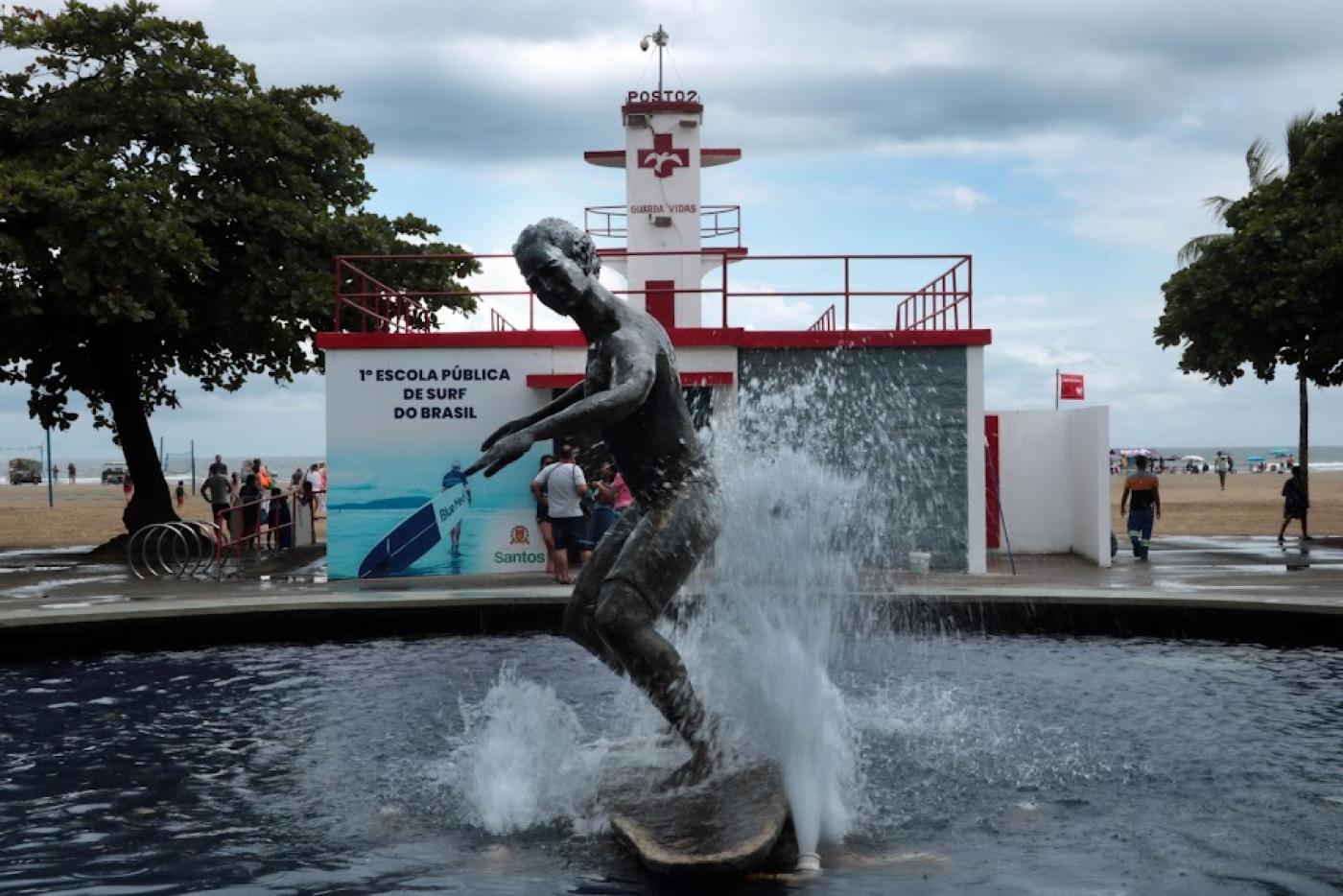 a fachada da escola de surfe com a estátua de surfista na água em primeiro plano. #paratodosverem 