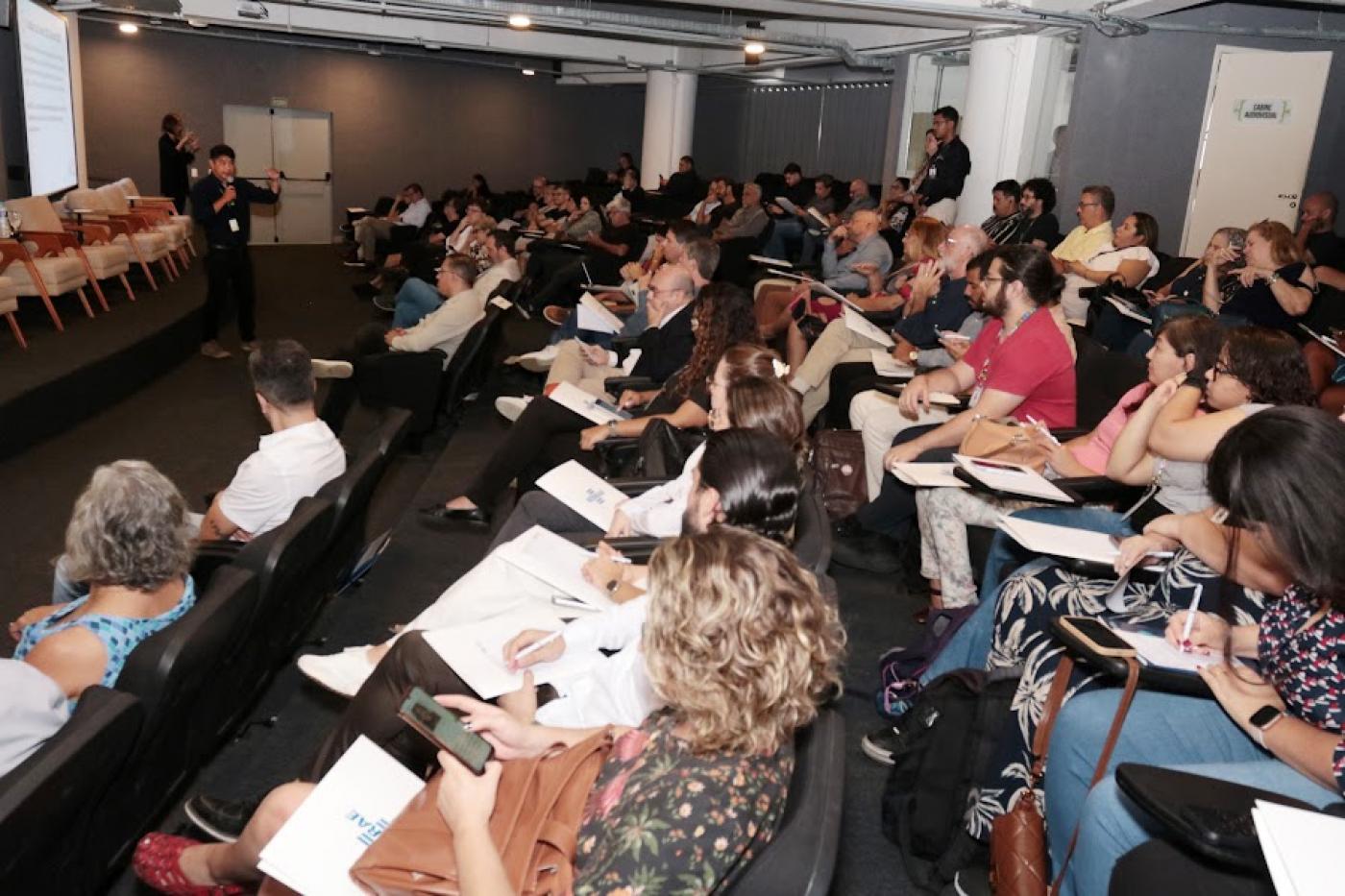 audiório com pessoas sentadas assistindo palestra. #paratodosverem