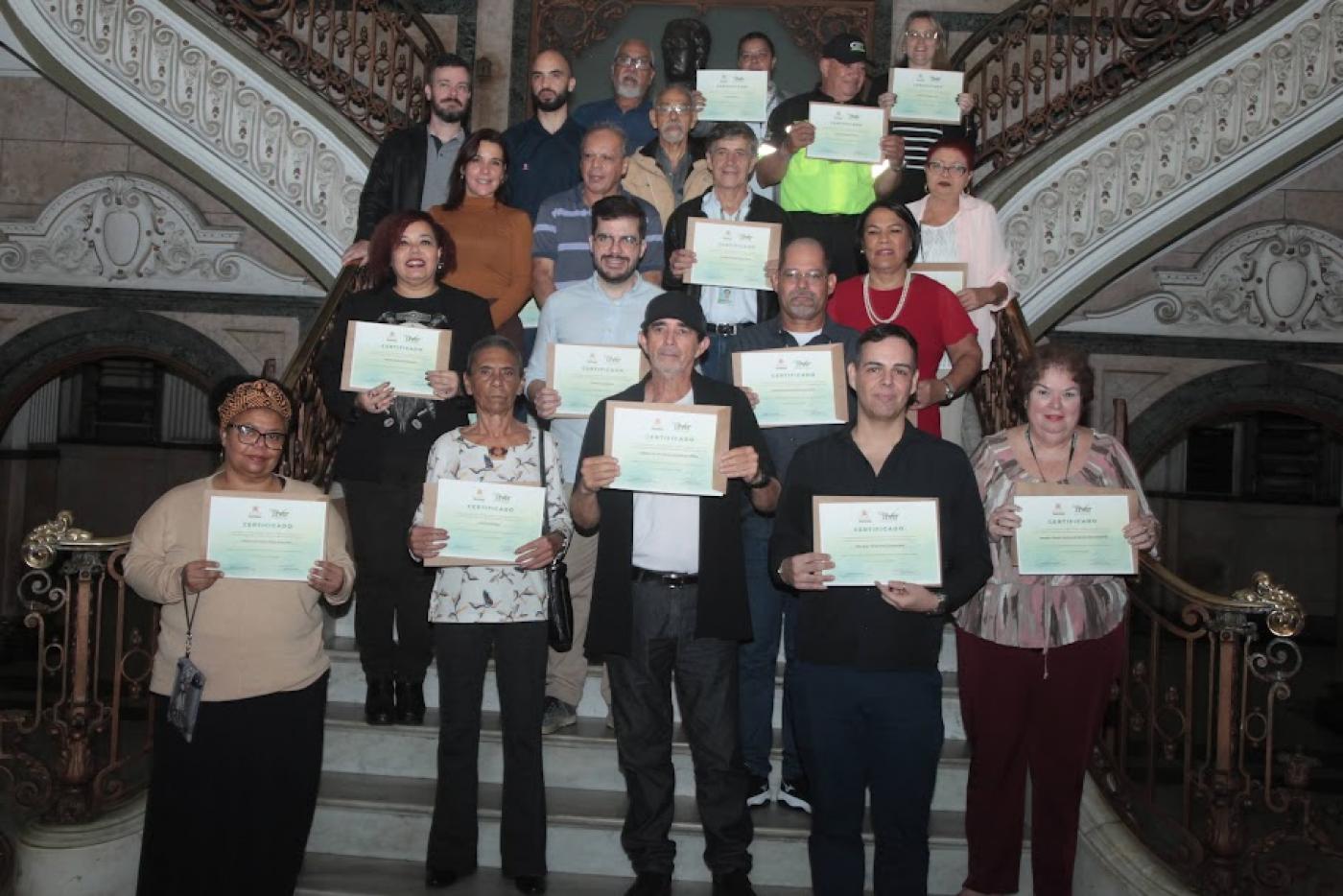 todos os homenageados posam para foto em escadaria do saguão da prefeitura. eles seguram seus respectivos certificados. #paratodosverem 