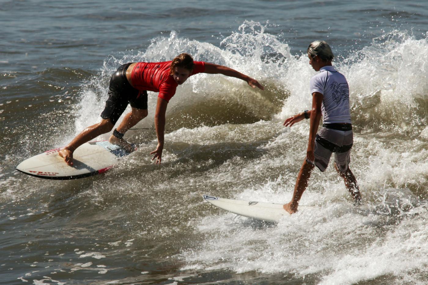 dois jovens estão surfando onda frente a frente. #paratodosverem 