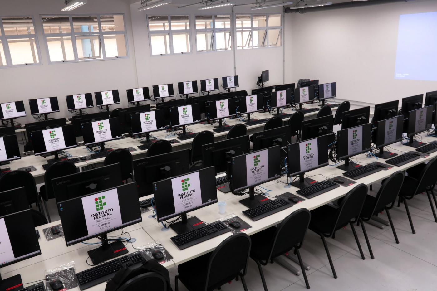 sala de aula com mesas e desktops. #paratodosverem