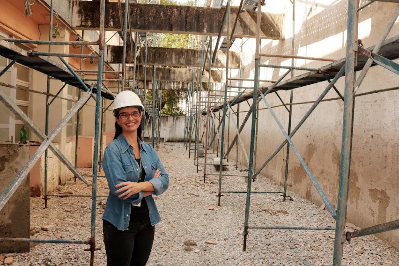 viviane está em pé, de braços cruzados, em ambiente de obra, com andaimes dos dois lados. #paratodosverem