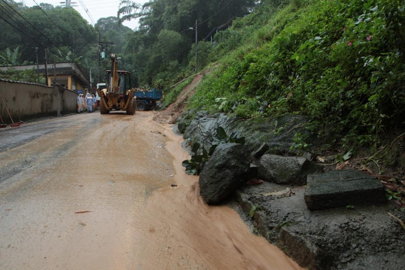 rua com deslizamento de terra do lado direito. Ao fundo, um trator para fazer limpeza 