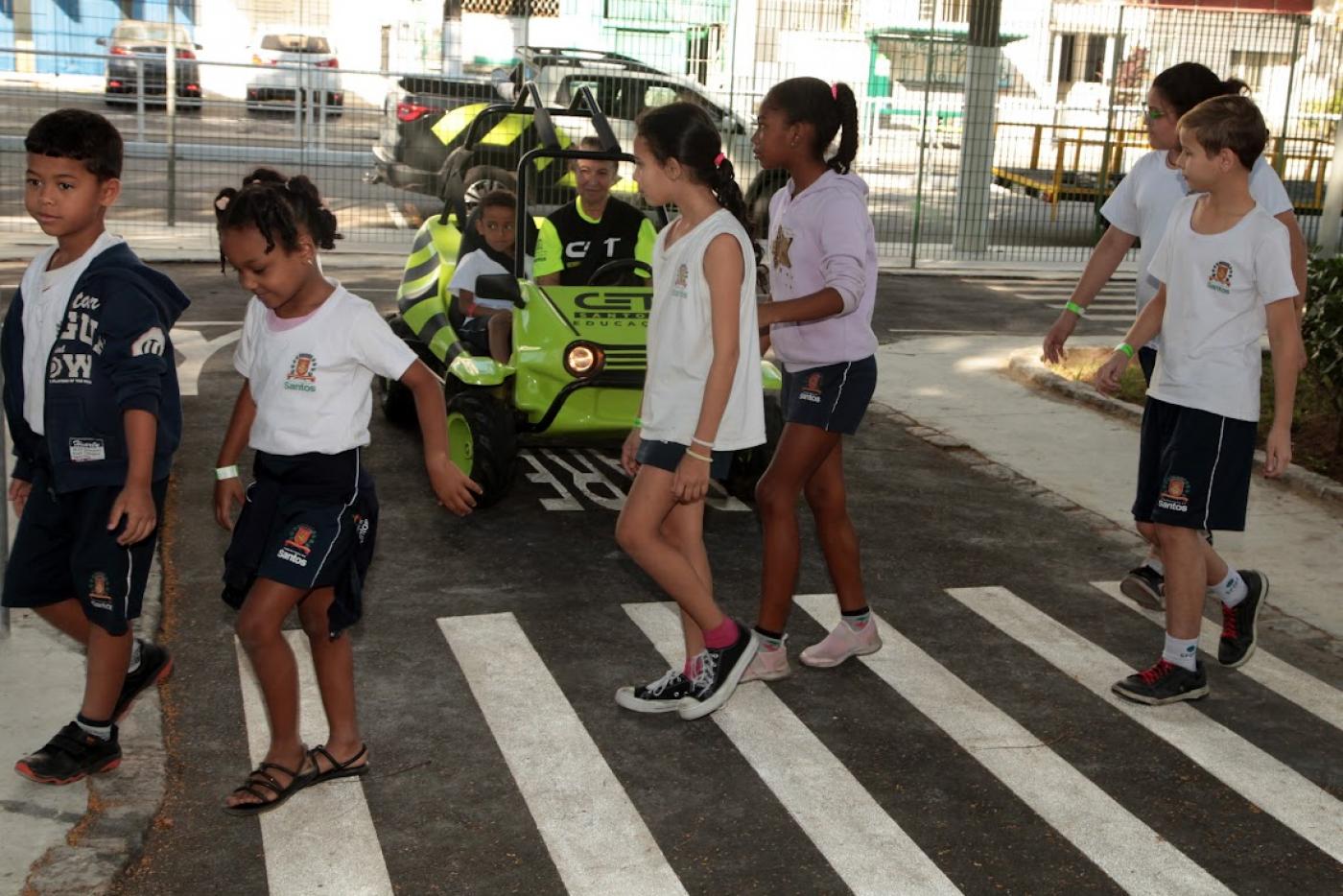 crianças atravessam a rua da minicidade de frente pra bugue que aguarda #paratodosverem