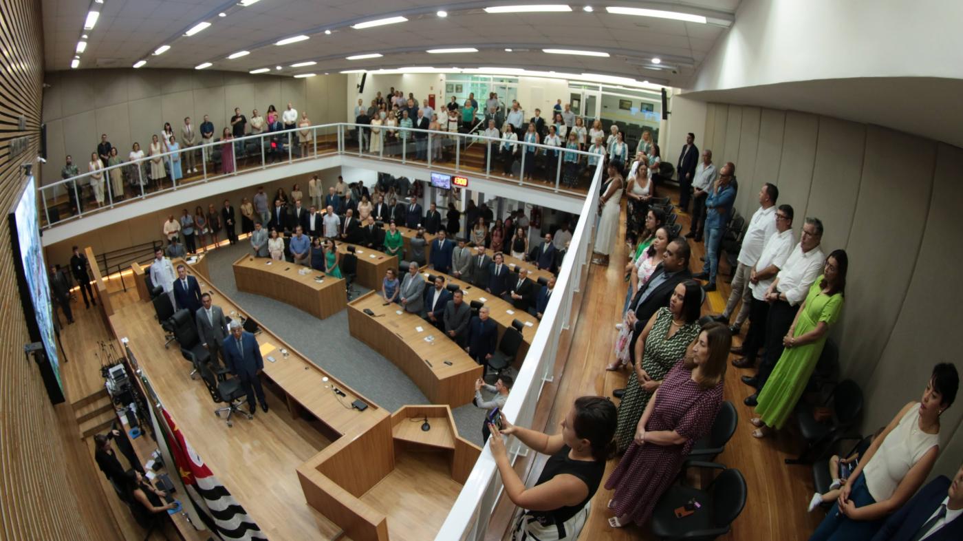 a tribuna da câmara municipal com público em pé cantando o hino nacional. #paratodosverem 