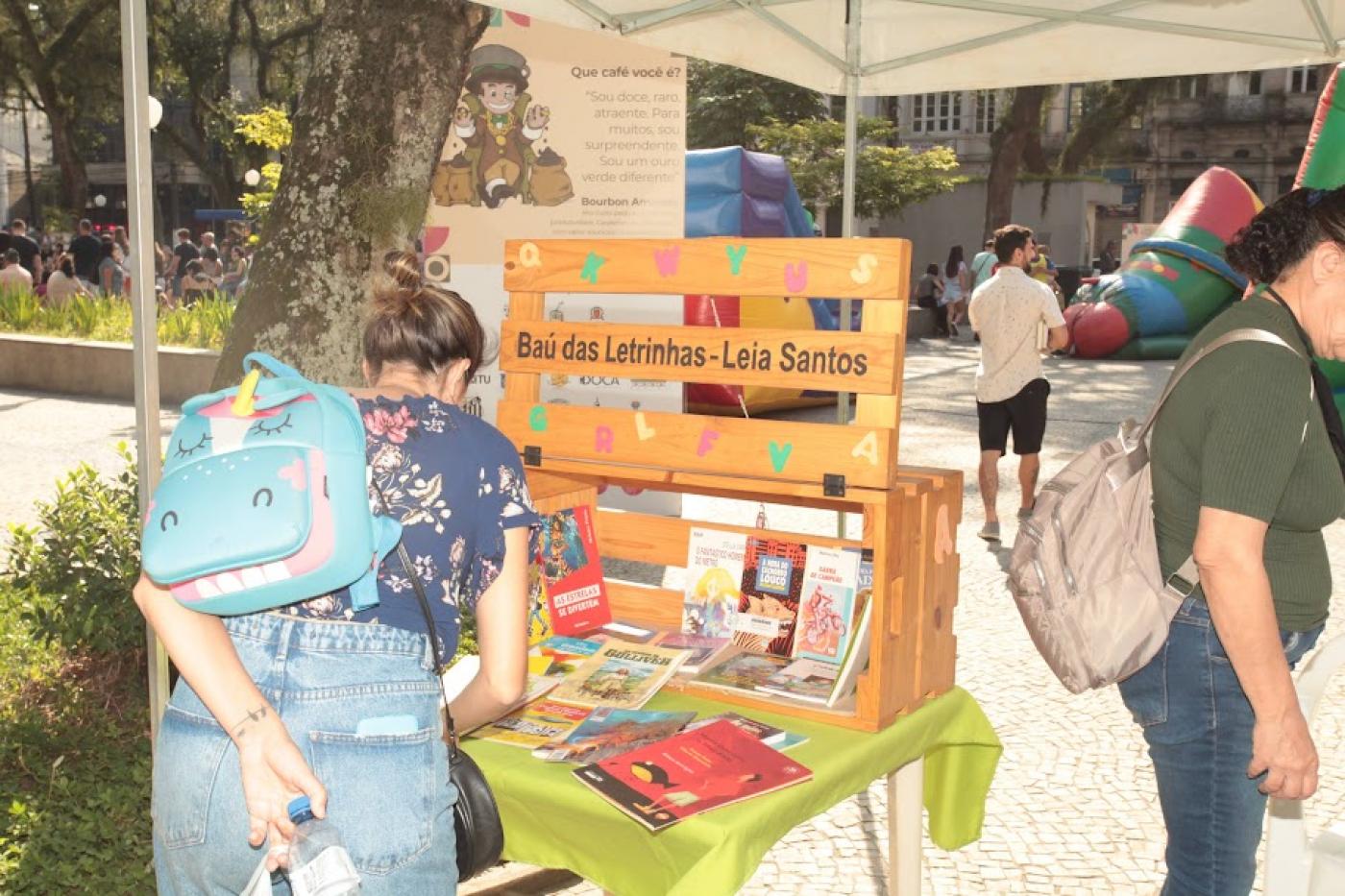 mulher de costas para foto mexe em livros dispostos sobre um estande. #paratodosverem 