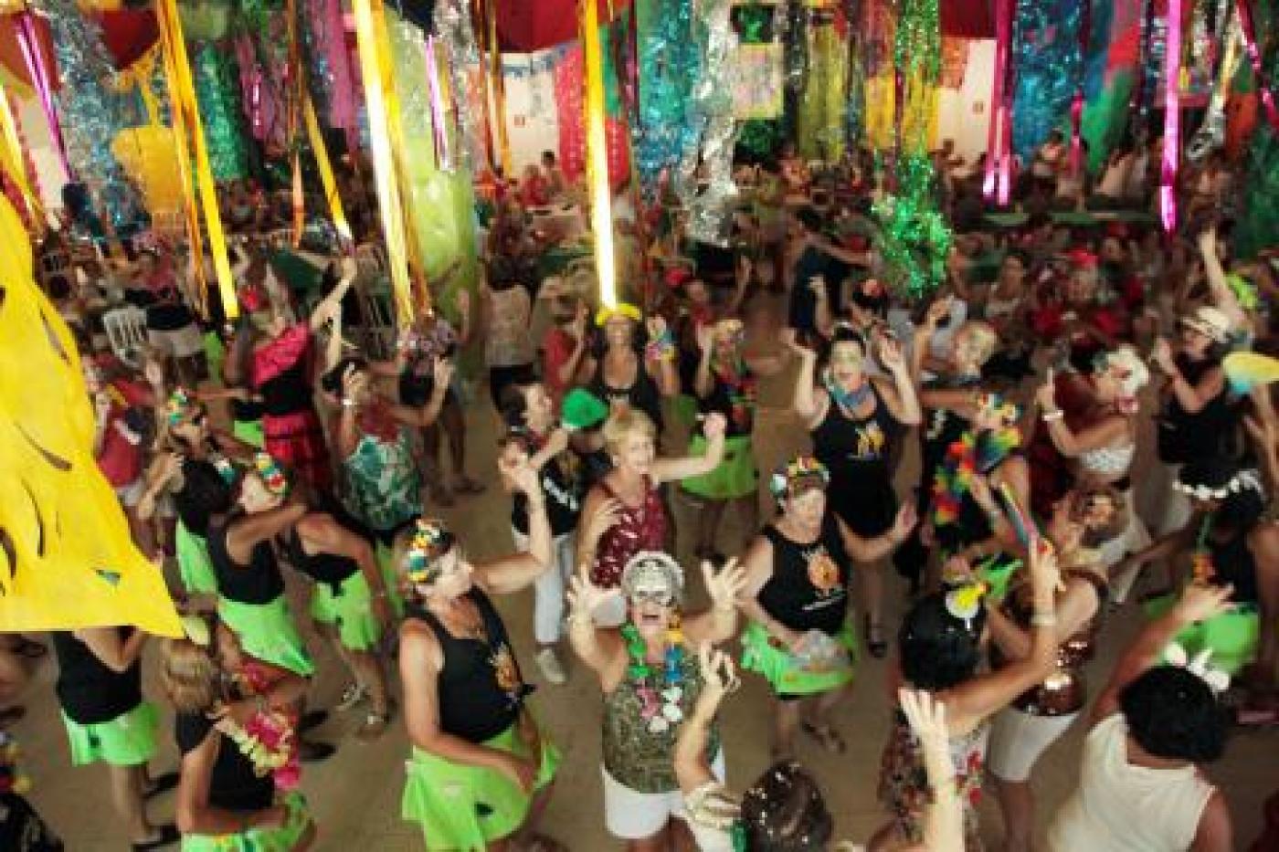 salão decorado com motivos de carnaval e pessoas dançando. #paratodosverem 