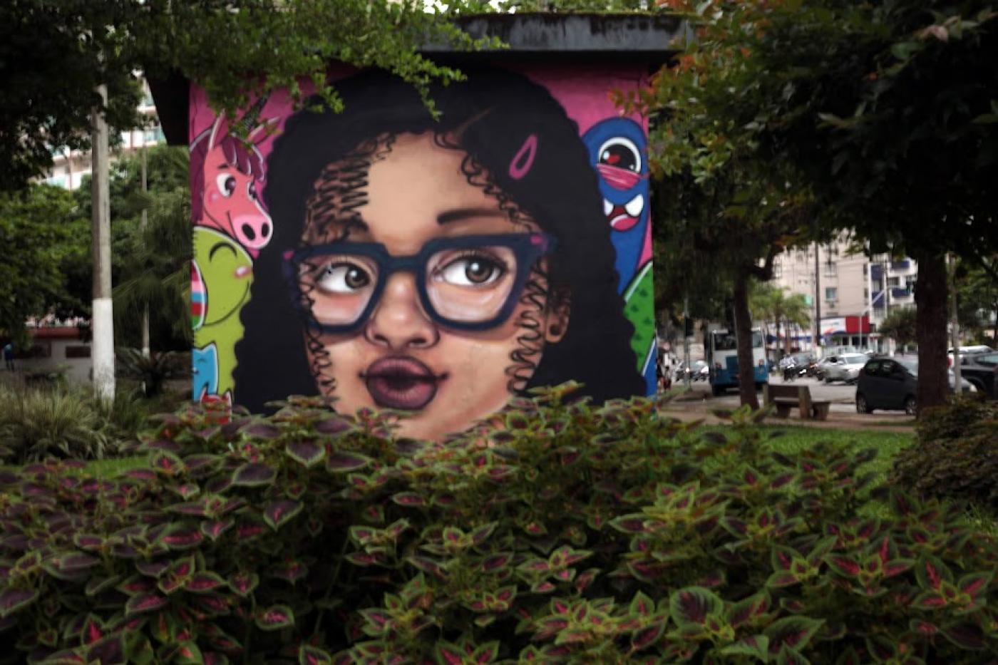 mural com rosto de criança negra usando óculos e motivos coloridos em torno do rosto. #paratodosverem 