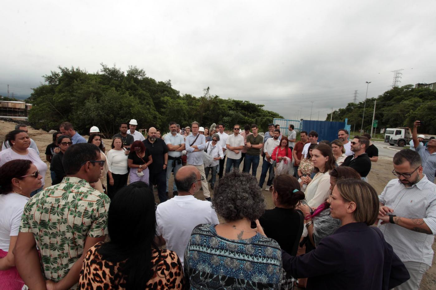 pessoas em pé em grupo num canteiro de obras, com morros ao fundo. #paratodosverem 