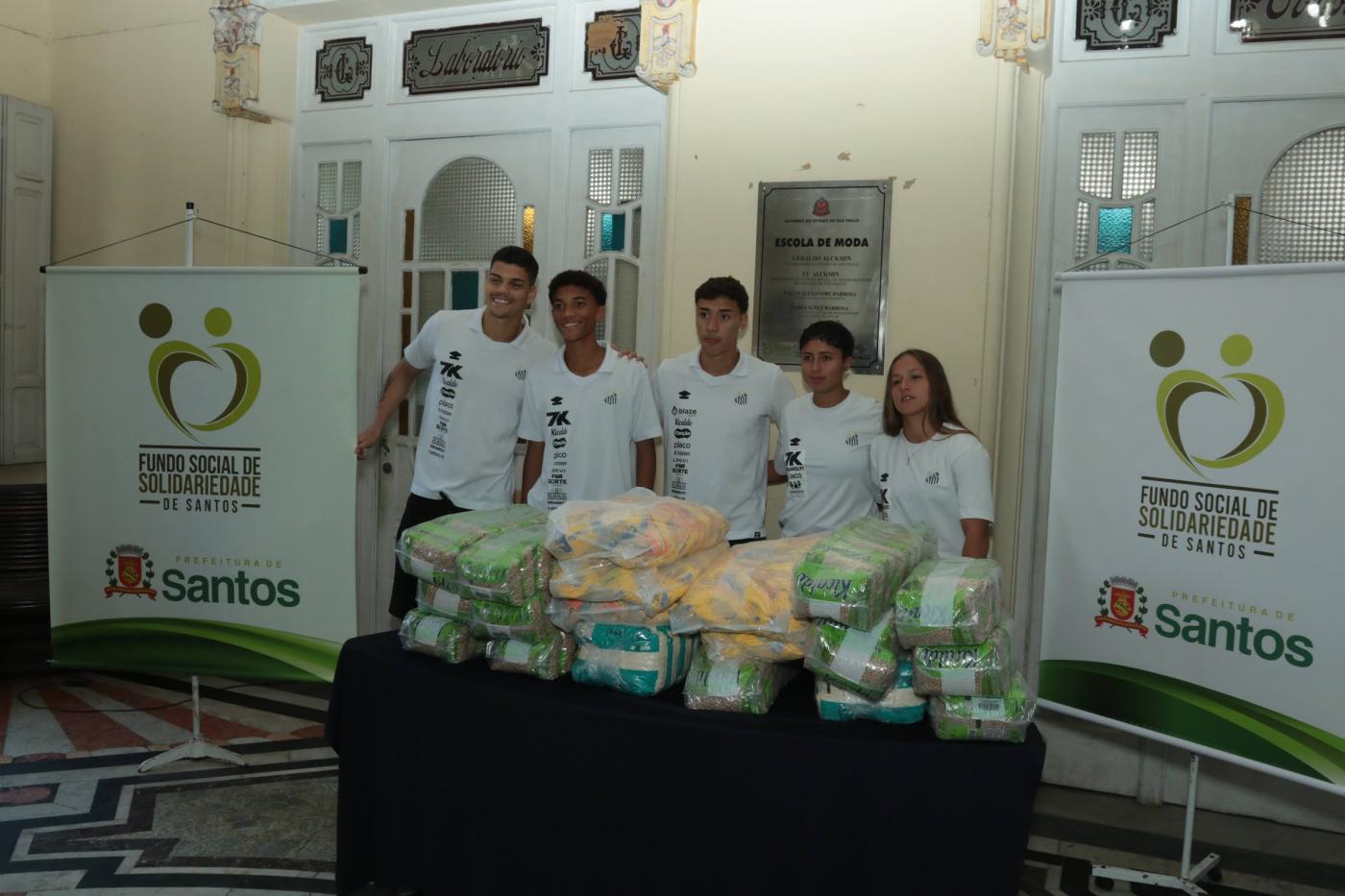 atletas do santos posam para foto atrás de mesa com mantimentos. #paratodosverem