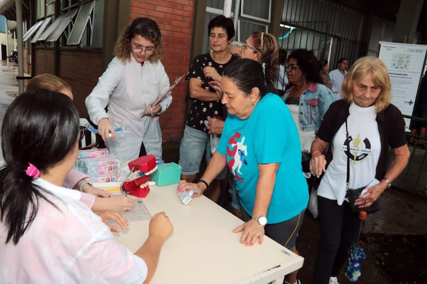 mulheres se juntam em torno de mesa ode há orientação sobre higiene bucal e entrega de kits. #paratodosverem 