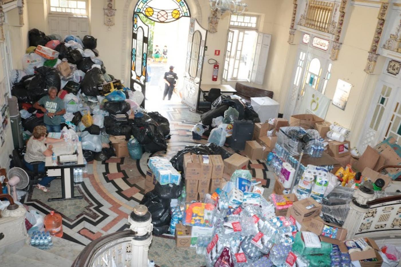 saguão do fundo social lotado de pacotes com mantimentos, água e itens de limpeza 