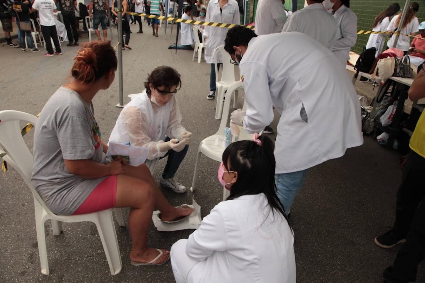 Voluntários fazem curativo no pé de uma mulher. #paratodosverem